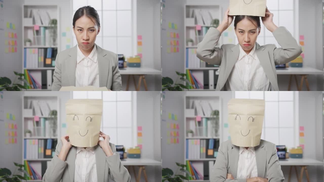 年轻的亚洲女商人坐在办公桌上穿着画微笑面具纸袋隐藏着在办公室工作失败的心情。