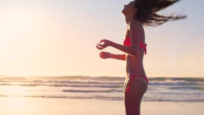 4k视频片段，一个迷人的年轻女子独自站在海滩上，在日落时玩弄头发