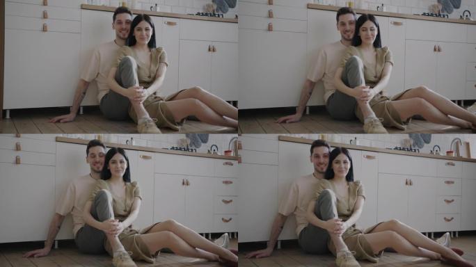 幸福的年轻夫妇坐在厨房的地板上微笑着看着相机的肖像