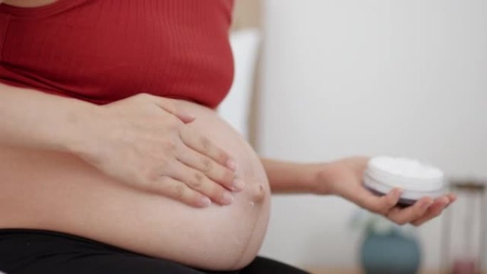 Pregnant woman applying skincare cream on her bell