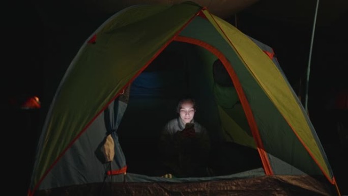 露营时，亚洲妇女晚上在帐篷里使用手机