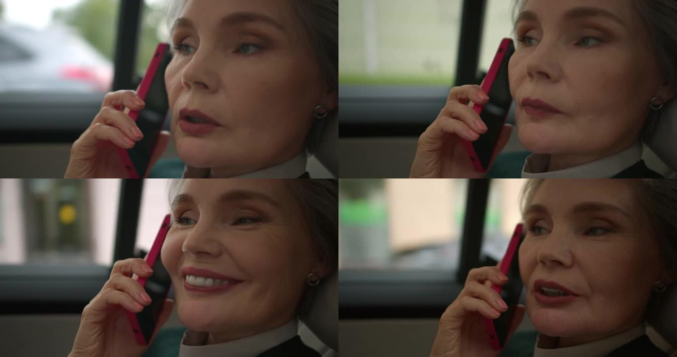 一位美丽的中年妇女微笑着在智能手机上讲话，作为乘客乘坐汽车的特写镜头