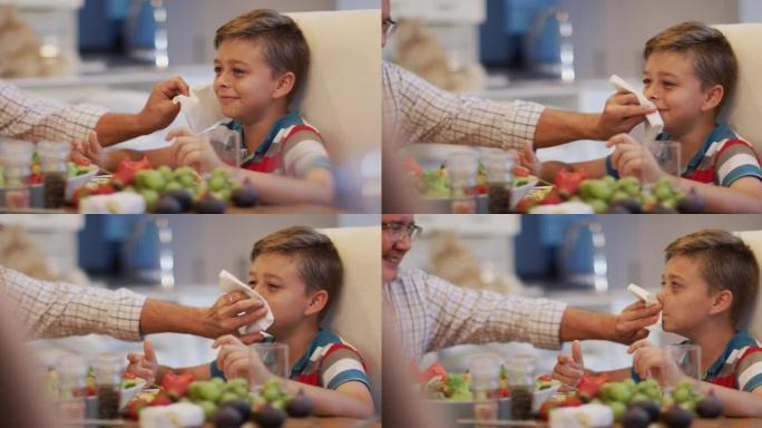 快乐的高加索祖父在餐桌上，在家庭用餐时擦孙子的脸