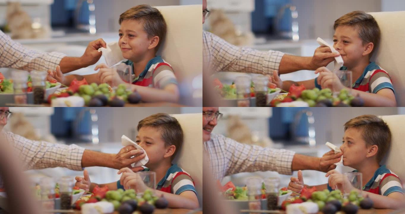 快乐的高加索祖父在餐桌上，在家庭用餐时擦孙子的脸