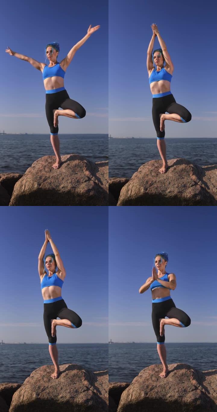 一位迷人的健美瑜伽老师，蓝色的头发穿着蓝黑色的瑜伽服，站在白天的天空和大海的背景下，她正在做树瑜伽姿