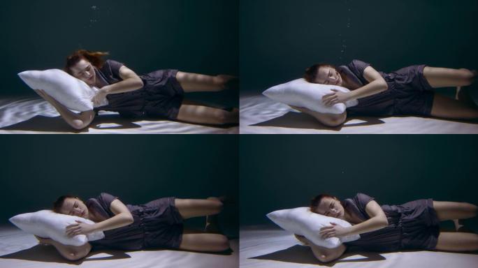 睡着了。穿着睡衣的年轻美女用枕头慢动作沉入水下的电影侧视图。