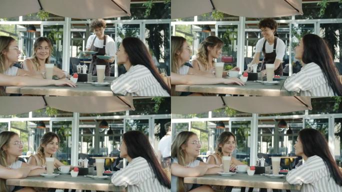 围裙的女服务员带甜点给一群在户外咖啡馆享受一天的年轻女性朋友