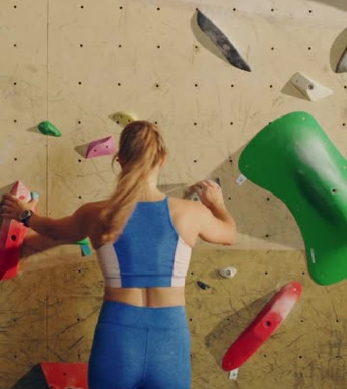 运动女攀岩者在健身房的抱石墙上练习单人攀爬的垂直肖像。女性在室内健身设施锻炼，进行极限运动生活方式训