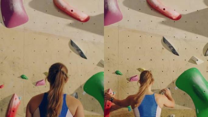 运动女攀岩者在健身房的抱石墙上练习单人攀爬的垂直肖像。女性在室内健身设施锻炼，进行极限运动生活方式训