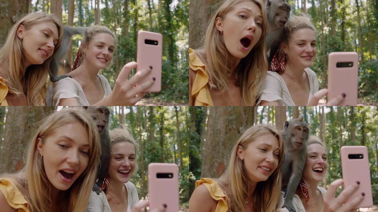 最好的朋友使用智能手机与猴子坐在肩膀上拍照两个女人在野生动物动物园与猴子合影，游客在巴厘岛旅行