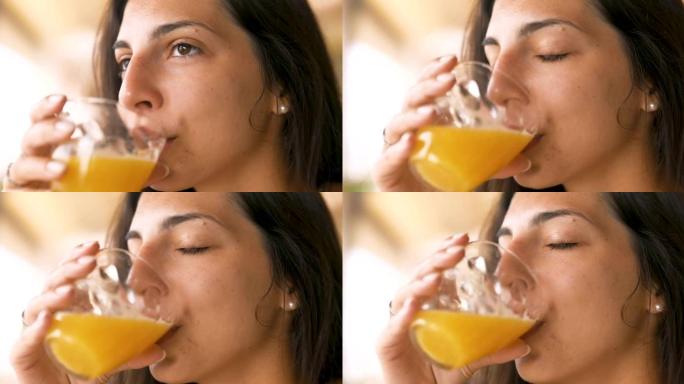一个年轻的黑发女人的真实特写镜头正在从透明玻璃杯中喝新鲜健康的饮食生物天然橙汁，早上吃早餐。