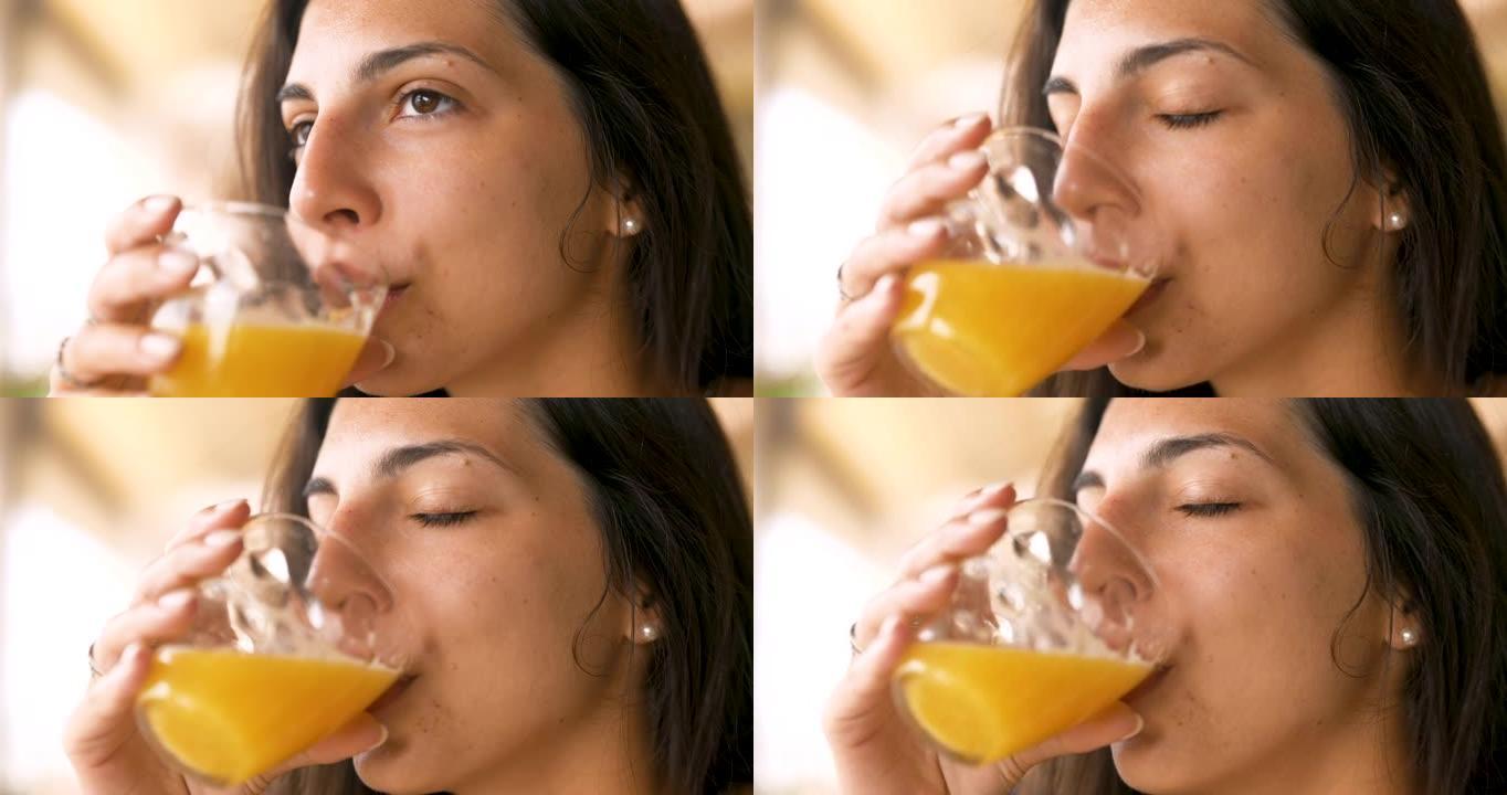 一个年轻的黑发女人的真实特写镜头正在从透明玻璃杯中喝新鲜健康的饮食生物天然橙汁，早上吃早餐。