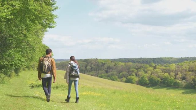 带着背包的夫妇在乡村森林边的小径上徒步旅行的后视图