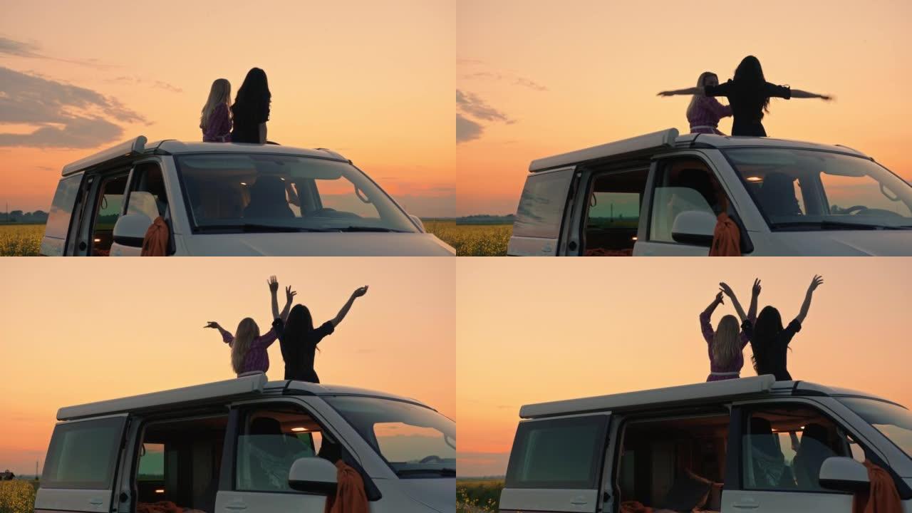 日落时分，两个女人在乡下露营者的屋顶上挥舞着手臂，玩得很开心。
