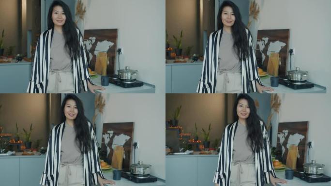 快乐的亚洲女人站在家里的厨房里穿着家装微笑的慢动作肖像