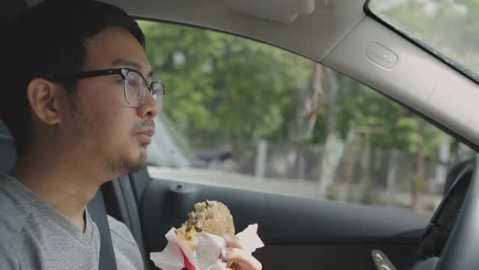 亚洲男子开车时吃汉堡