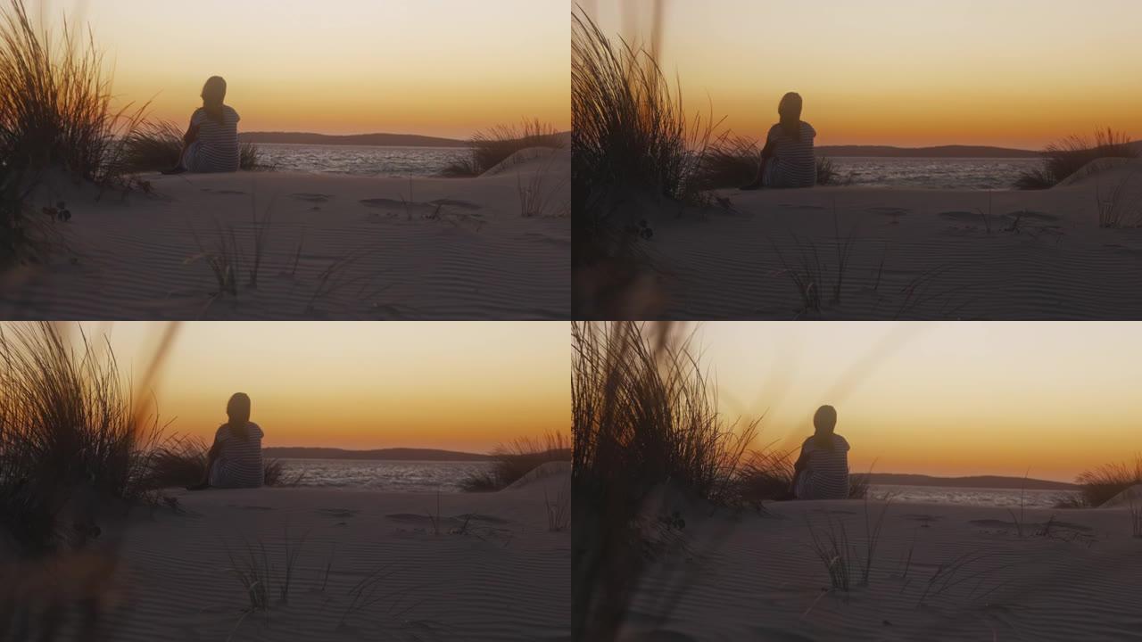日落时独自坐在海滩上的女人的慢动作视图。