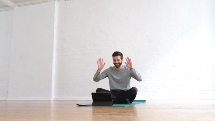 坐在瑜伽垫上的男人在瑜伽课上挥舞着他的数字平板电脑