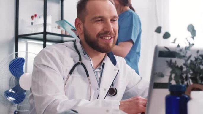 快乐微笑的白人男性医生穿着实验室外套，听诊器通过笔记本电脑网络摄像头视频在线与远程客户交谈。