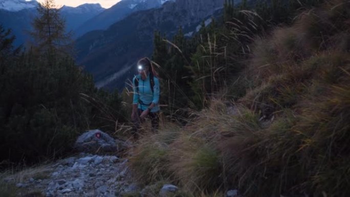 年轻的女徒步旅行者在黄昏时带着头灯在落基山小径上徒步旅行时欣赏着令人难以置信的景色