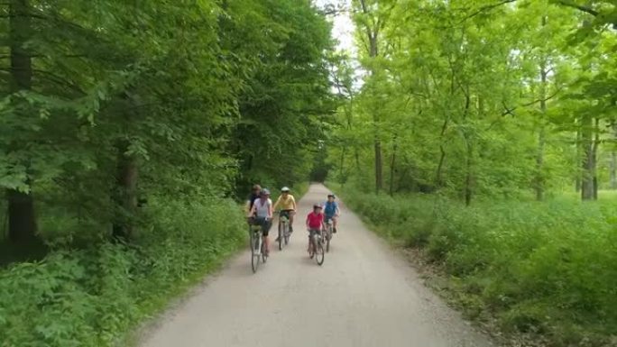 有三个孩子的空中家庭在穿过森林的道路上骑自行车