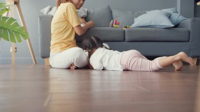 快乐快乐的亚洲家庭妈妈追逐她可爱的烦躁的孩子，她在地板上爬行，在家里的客厅放松。