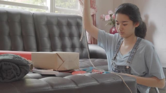 亚洲年轻少女制作手工物品护理包。可爱的女孩打包一个包装箱，准备从远处寄给她的家人或朋友。