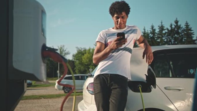 一个年轻人的SLO MO肖像在停车场充电时使用智能手机