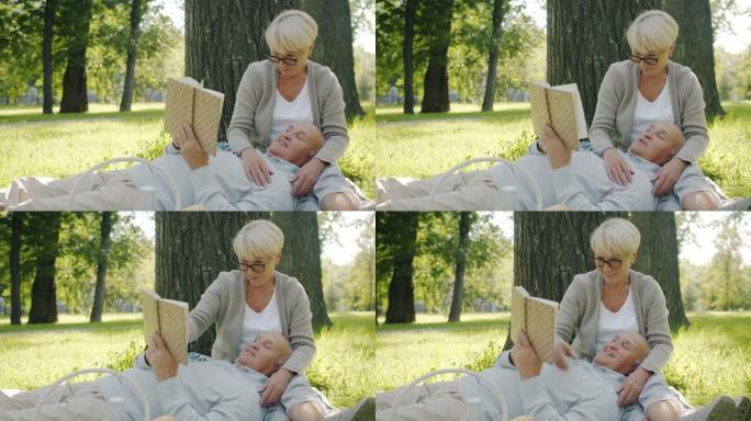 快乐的老年夫妇在公园的草坪上看书和大笑的慢动作肖像
