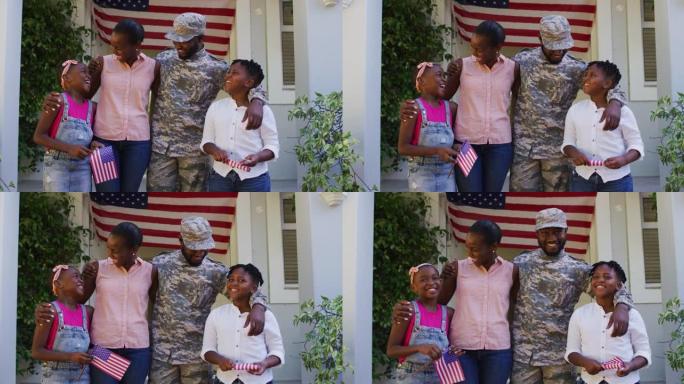 快乐的非裔美国男性士兵在房屋和美国国旗前拥抱妻子和孩子