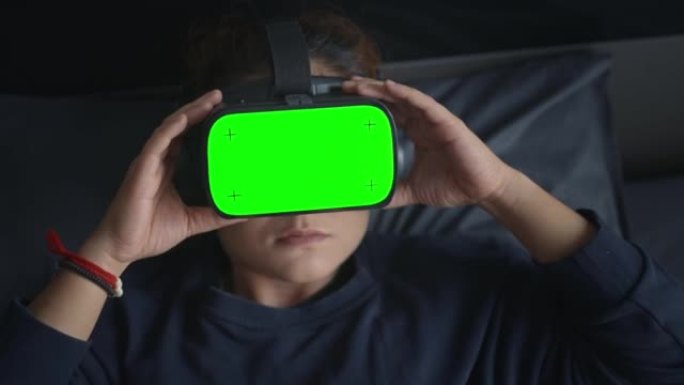 女人在VR耳机上戴着色度键绿屏躺在床上