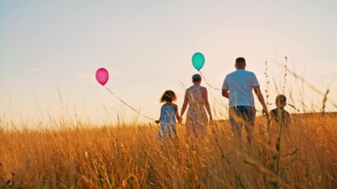 有两个孩子的SLO MO家庭在黄金时段在高高的羊茅草中行走时拿着气球