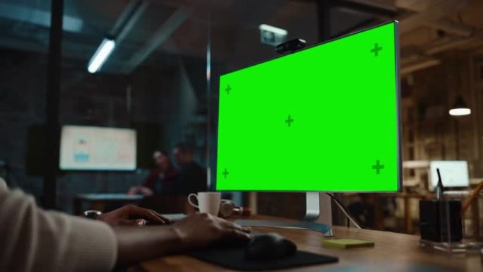 在繁忙的创意办公室中，一位黑人非裔美国人项目经理在台式计算机上进行视频通话，并带有绿屏模拟显示。男性