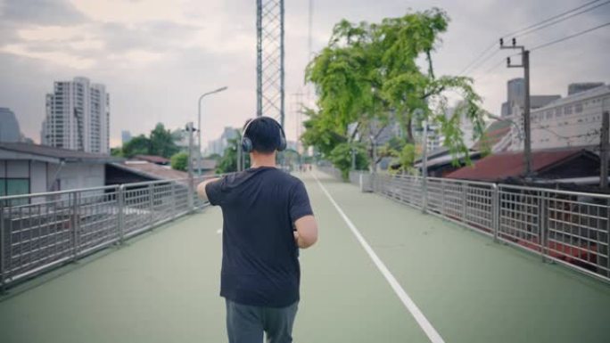 迷人的亚洲成年男子在城市跑步或慢跑。进行运动训练的男性通过在早上进行街头城市跑步来挑战自己。