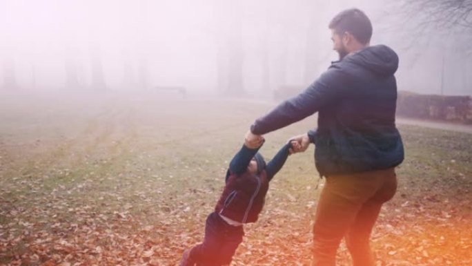 父亲在雾笼罩的秋天公园里旋转儿子