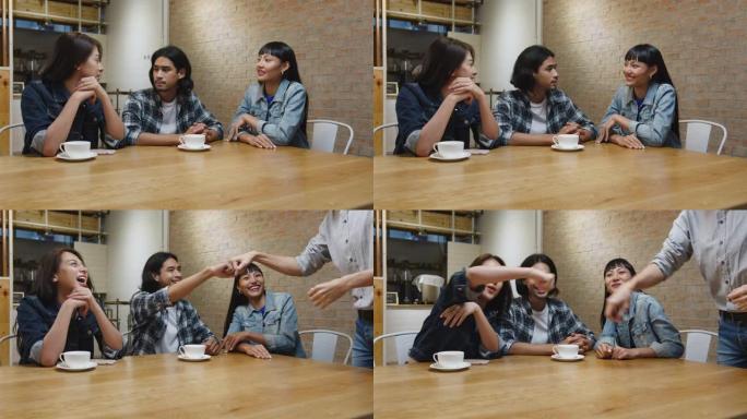 一群快乐的亚洲年轻朋友一起坐在咖啡馆餐厅，玩得开心，用友谊拳头打气问候。