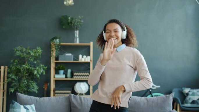 快乐非裔美国学生美女戴着耳机在家跳舞唱歌
