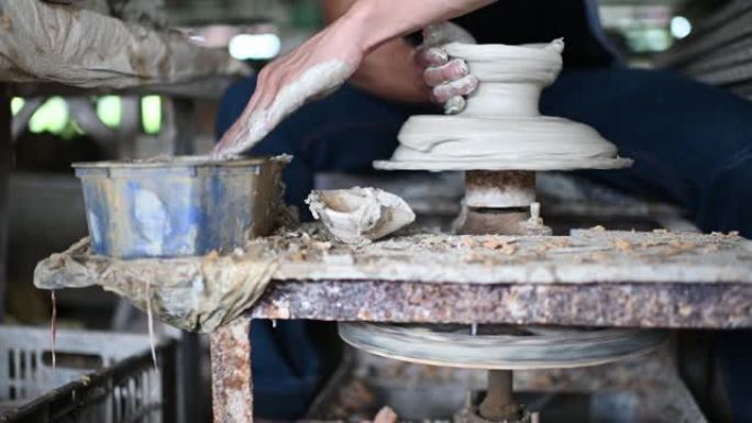 亚洲华人一名男子陶工在他的车间里工作，他带着旋转陶轮