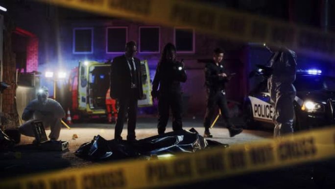 放大到夜间的犯罪现场:犯罪现场调查小组工作在谋杀。女警官向侦探介绍受害者的尸体。法医和护理人员在工作