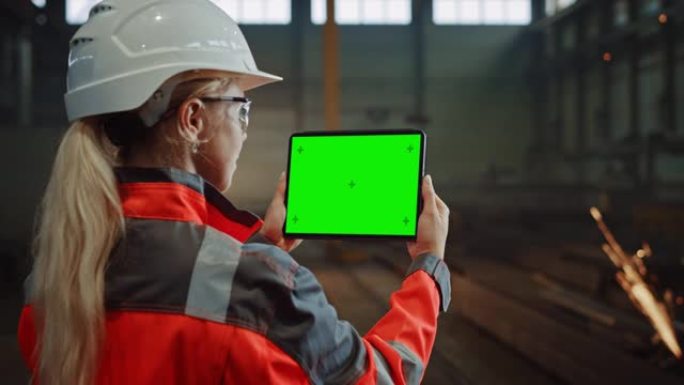 专业的重工业工程师使用带有绿屏模拟显示的平板电脑。在金属制造仓库工作的女性工业专家，背景是火花。