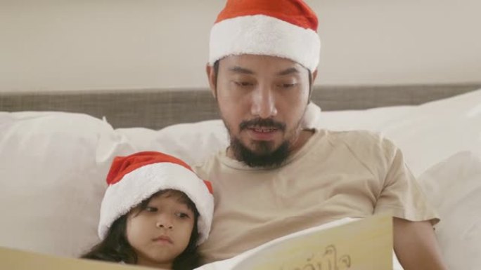 亚洲父亲正在卧室里和女儿一起读圣诞节童话。