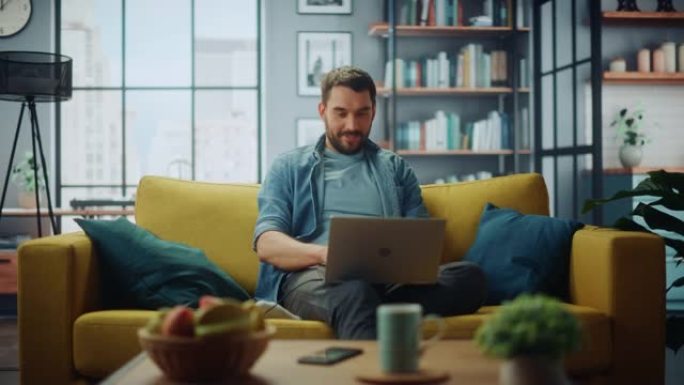 英俊的白人男子坐在时尚舒适的客厅的沙发上，在笔记本电脑上工作。自由职业者在家工作。浏览互联网，使用社