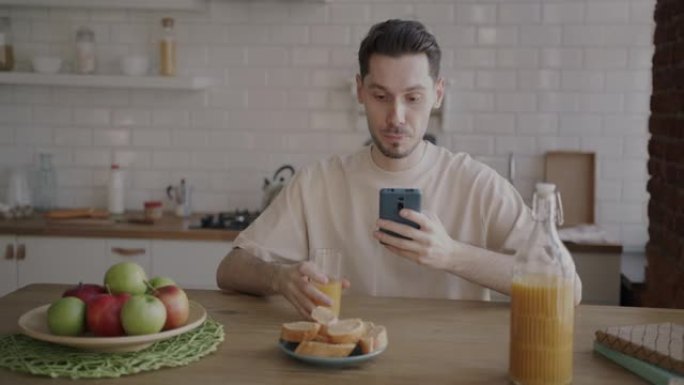 年轻人在家里的厨房里喝果汁和使用智能手机的肖像