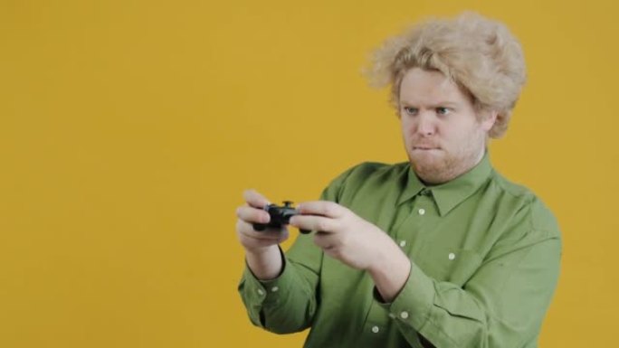 兴奋的家伙在黄色背景上使用操纵杆获胜玩视频游戏的肖像