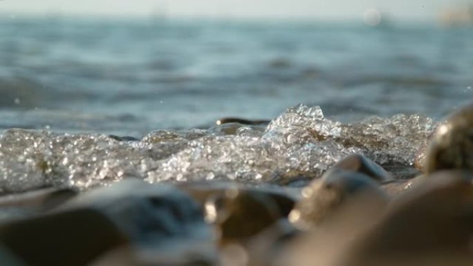 特写: 玻璃状的海水溅到空旷的海岸的棕色鹅卵石上。