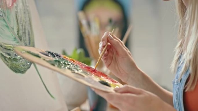 一位女画家在工作室的画布上作画的特写镜头。一个女孩的手在工作坊的艺术品调色板上混合颜色。艺术家在工作