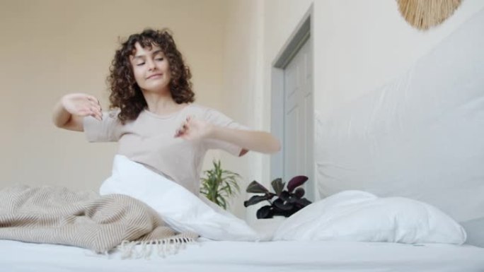 放松的年轻女士在舒适的床上醒来的肖像微笑着伸展手臂和身体