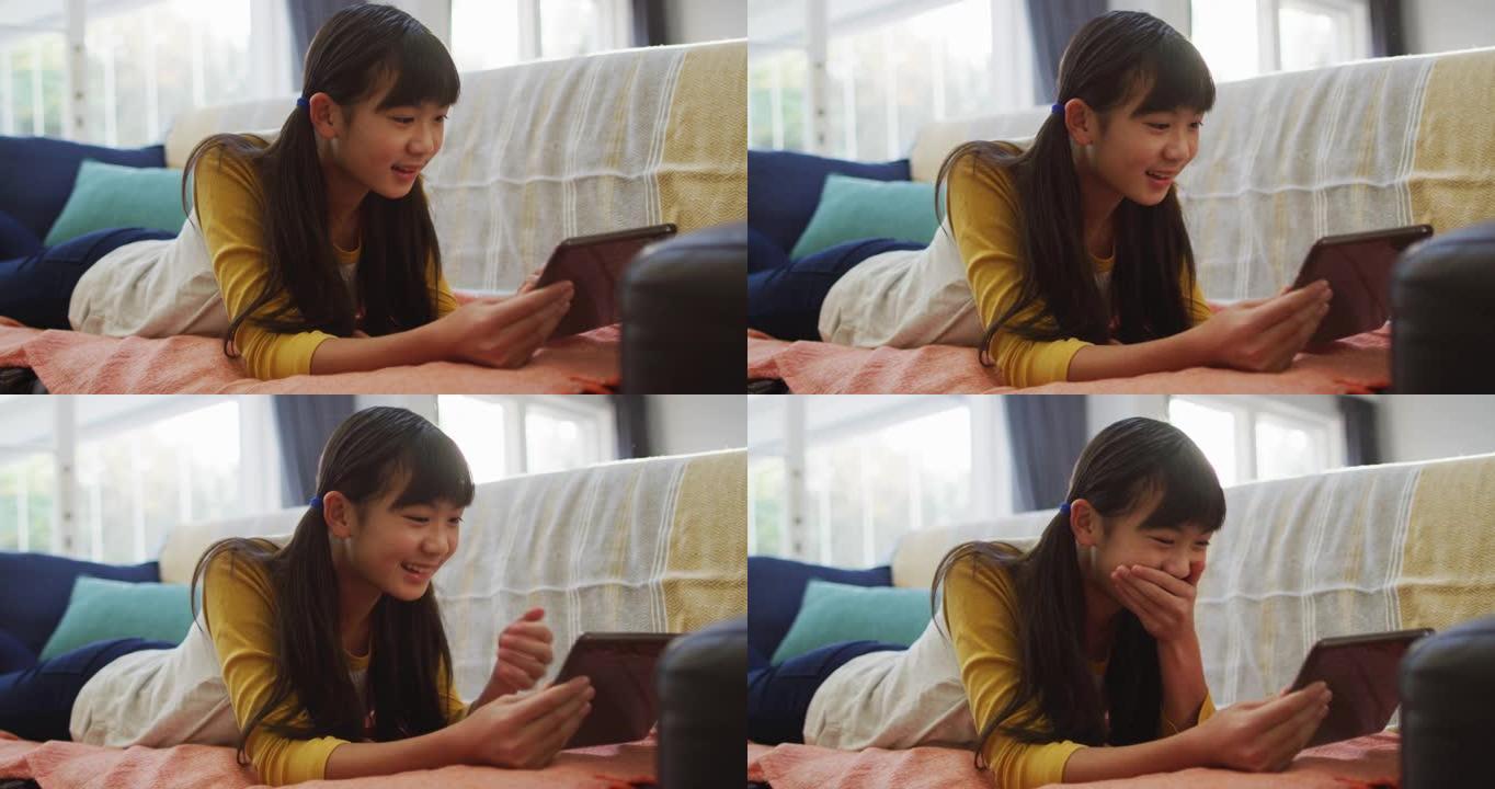 亚洲女孩微笑着用平板电脑躺在家里的沙发上