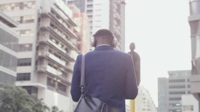 有趣的商人喜欢听音乐和在现代企业商业区散步。年轻的非洲裔美国男性在工作成功后在市区市区享受激励音频