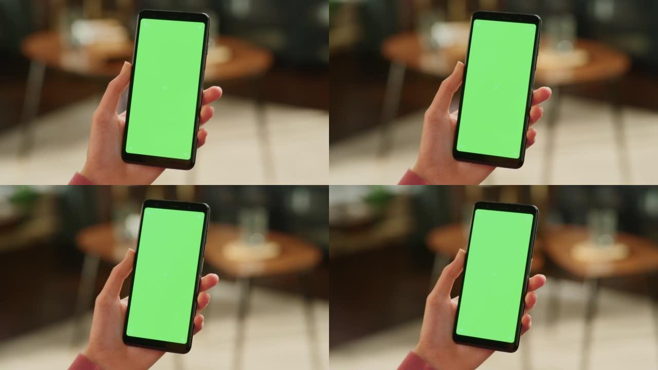 女性手握着带有绿屏模拟显示的智能手机。女性在家里休息，在移动设备上观看视频和阅读社交媒体帖子。特写镜